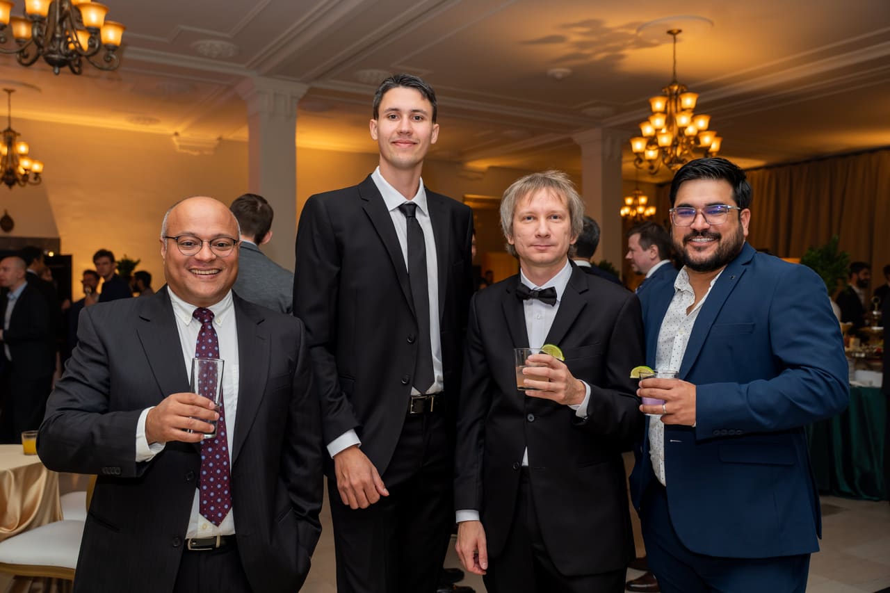 Four colleagues in suits standing together with drinks at the gala