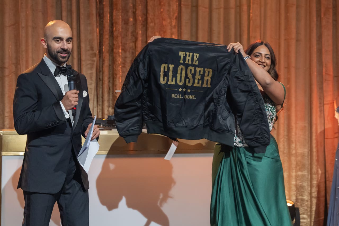 A colleague on stage presenting a jacket embroidered “The Closer”